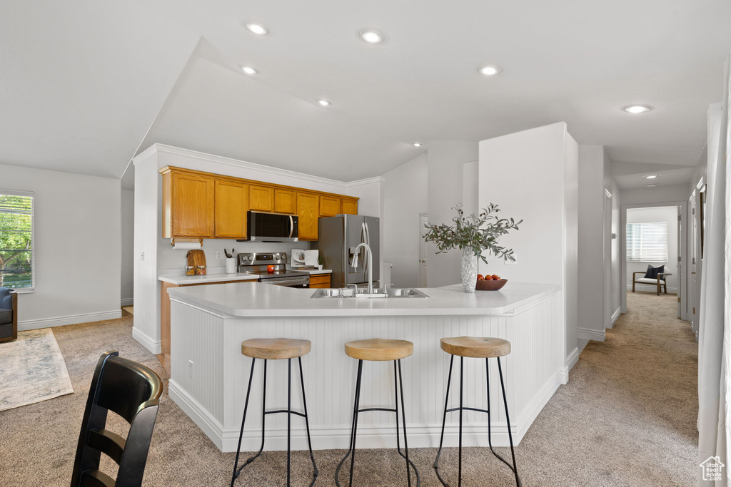 Kitchen with lofted ceiling, a kitchen bar, stainless steel appliances, and light carpet