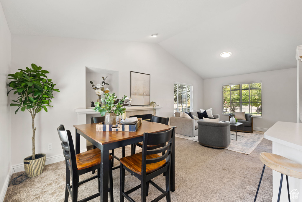 Dining area with a fireplace, light carpet, and vaulted ceiling