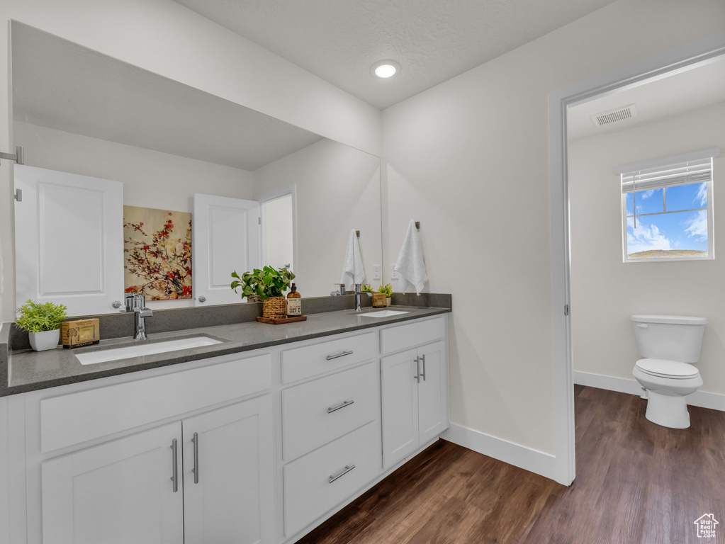 Full bath with double vanity, baseboards, toilet, wood finished floors, and recessed lighting