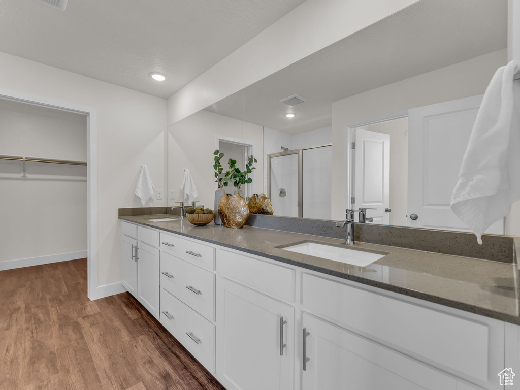 Full bathroom with a stall shower, double vanity, wood finished floors, baseboards, and a walk in closet