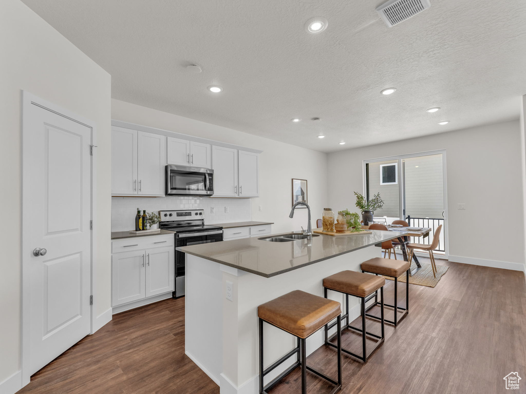 Kitchen with appliances with stainless steel finishes, a sink, a kitchen breakfast bar, dark wood-style flooring, and a kitchen island with sink