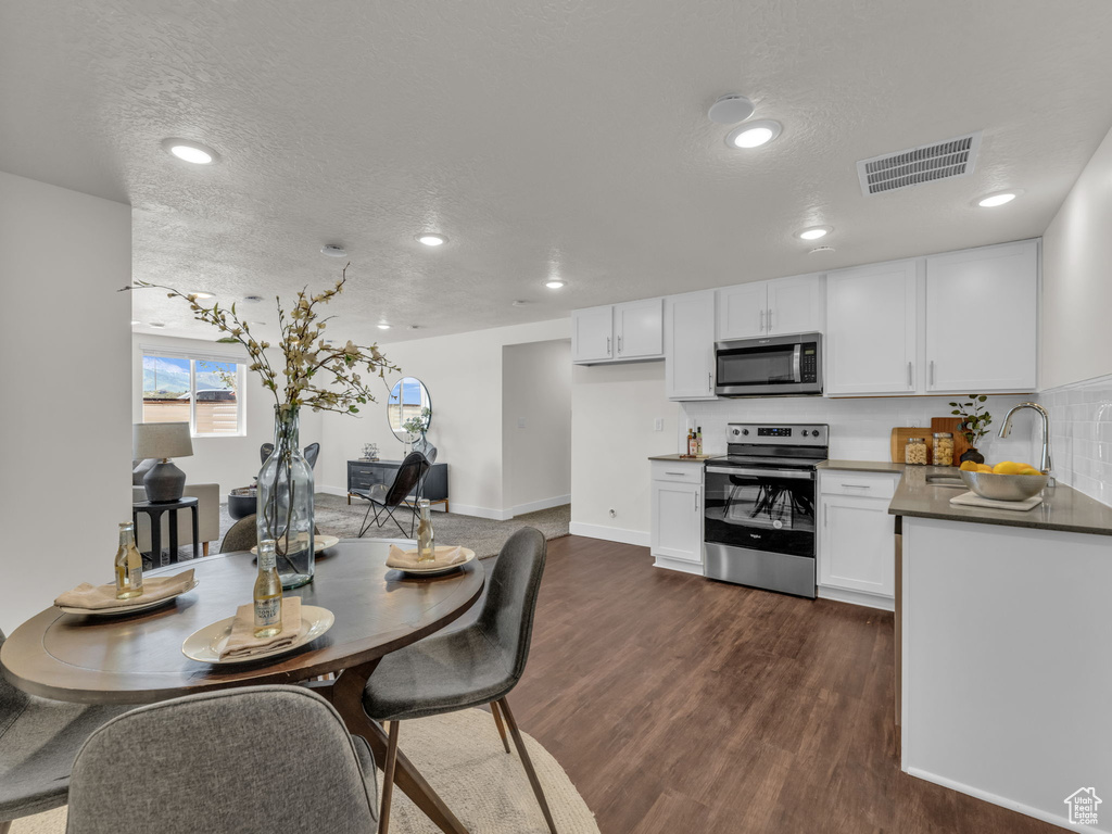 Kitchen with appliances with stainless steel finishes, white cabinets, dark wood-style flooring, a textured ceiling, and dark countertops