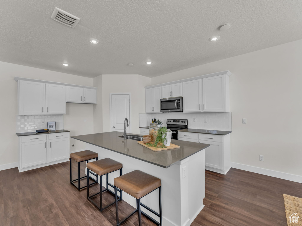 Kitchen with stainless steel appliances, dark countertops, a sink, dark wood-style floors, and a textured ceiling