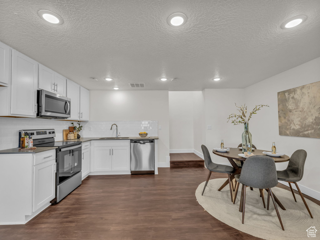 Kitchen featuring appliances with stainless steel finishes, a sink, backsplash, a textured ceiling, and dark wood-style flooring
