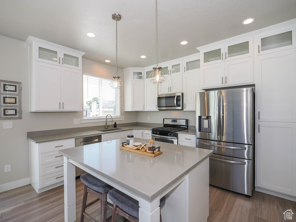 Kitchen featuring white cabinets, a center island, decorative light fixtures, stainless steel appliances, and dark hardwood / wood-style flooring