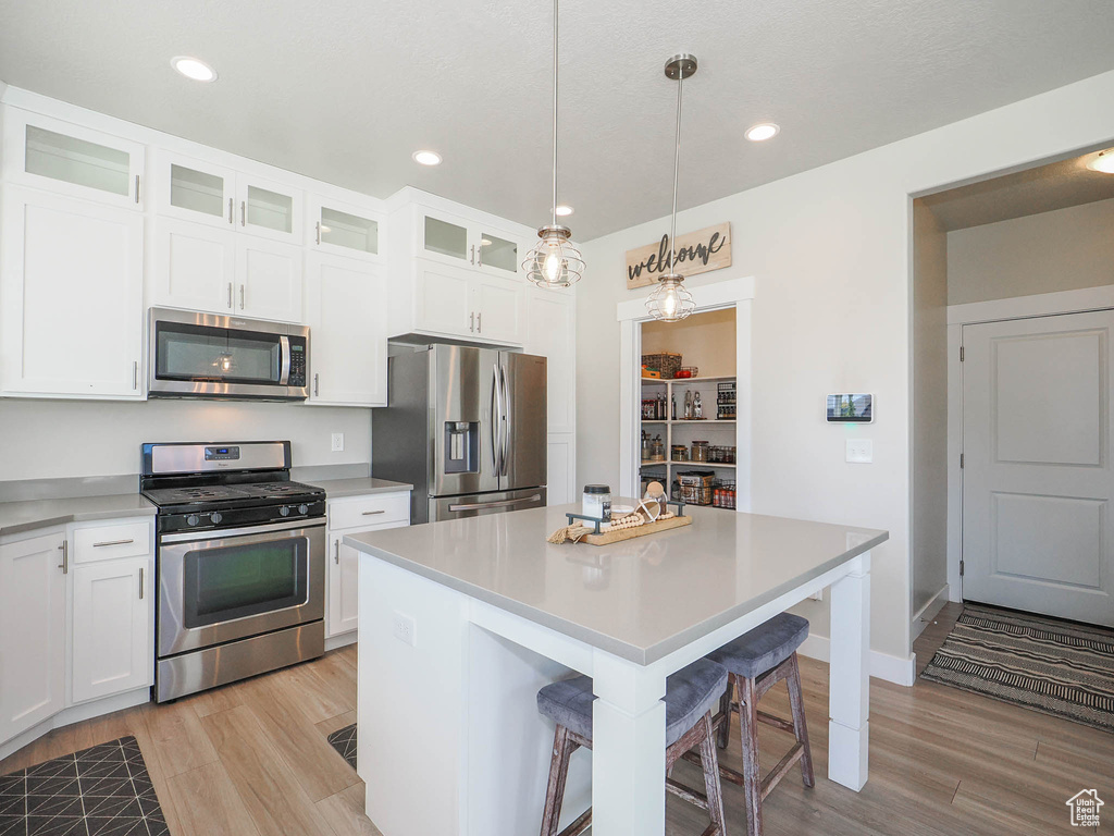 Kitchen featuring a kitchen island, stainless steel appliances, light wood-type flooring, and white cabinetry