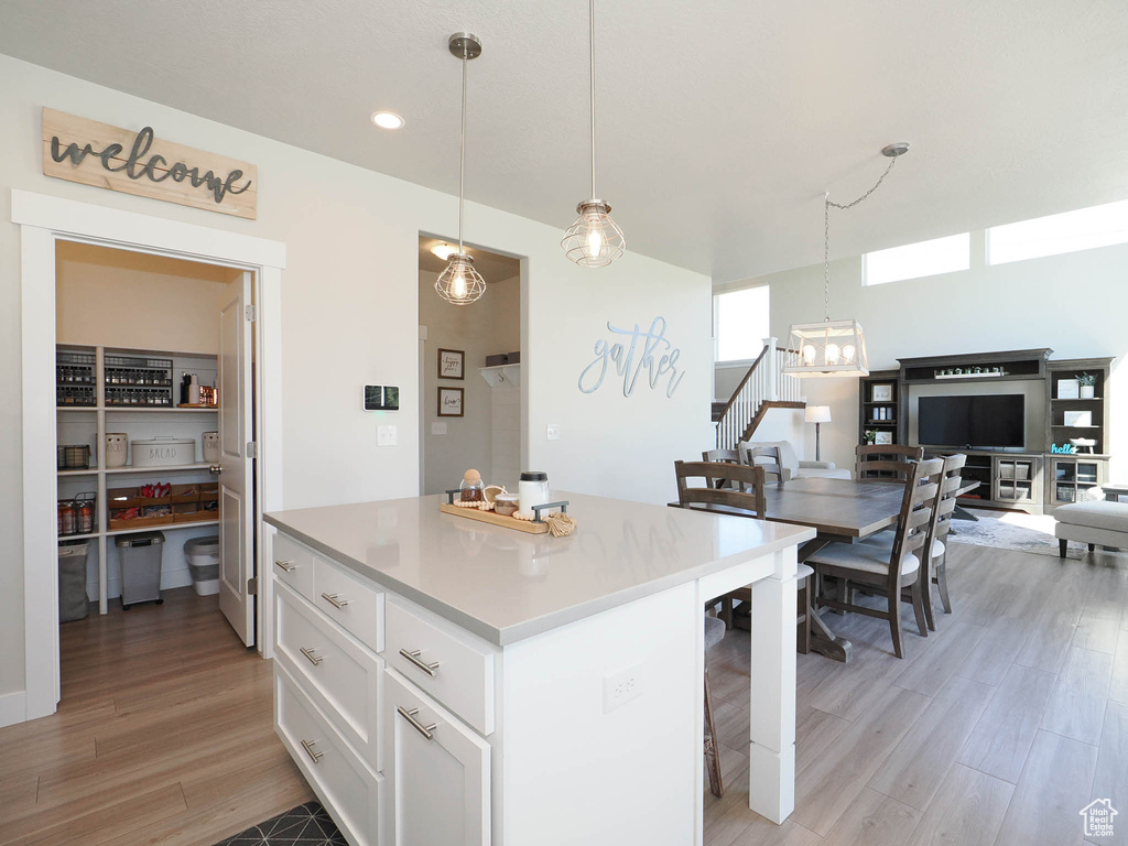 Kitchen with a kitchen bar, hanging light fixtures, white cabinets, and light hardwood / wood-style floors