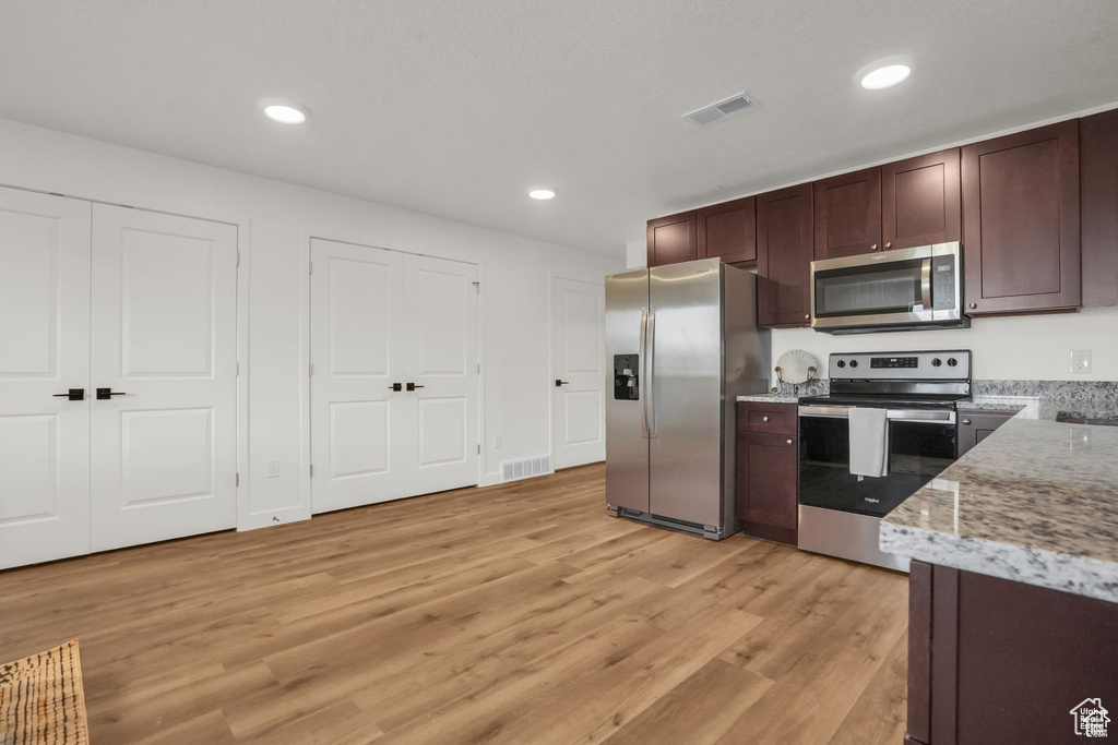 Kitchen featuring appliances with stainless steel finishes, light stone counters, and light hardwood / wood-style floors