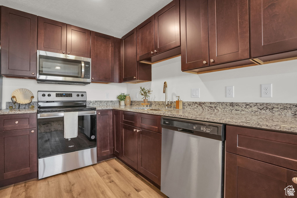 Kitchen with sink, light stone countertops, appliances with stainless steel finishes, and light hardwood / wood-style floors