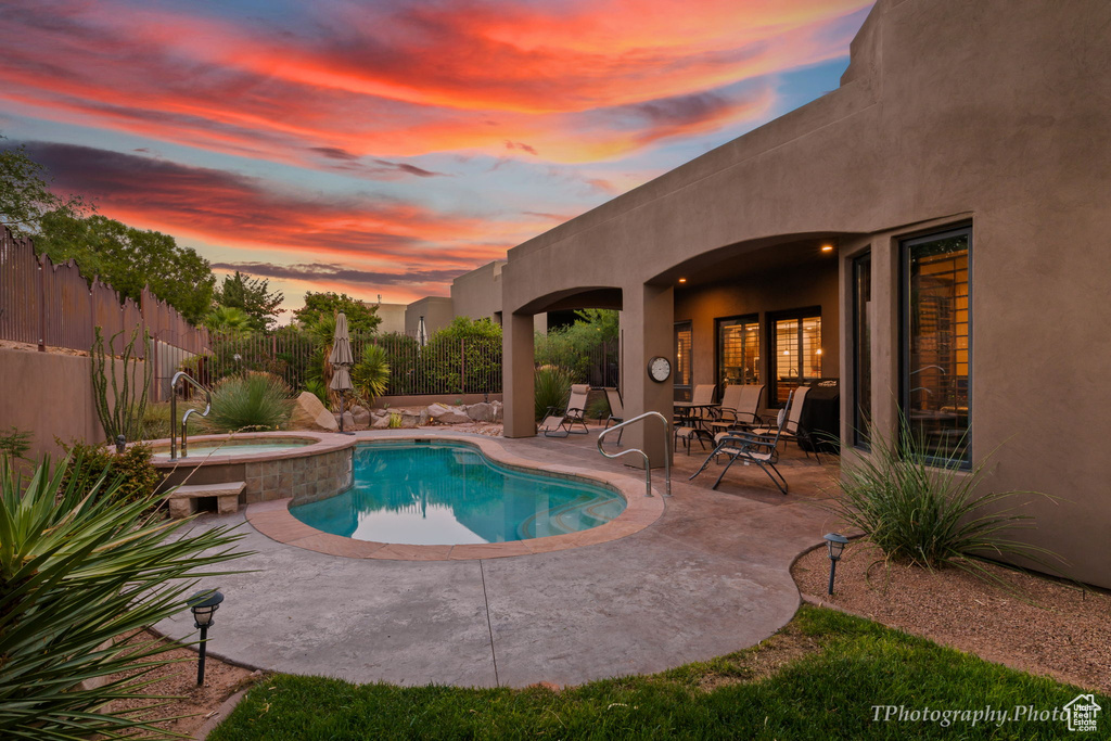 Pool at dusk with an in ground hot tub and a patio