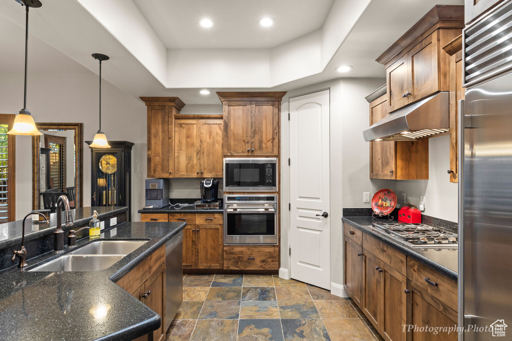 Kitchen with a raised ceiling, built in appliances, decorative light fixtures, and sink