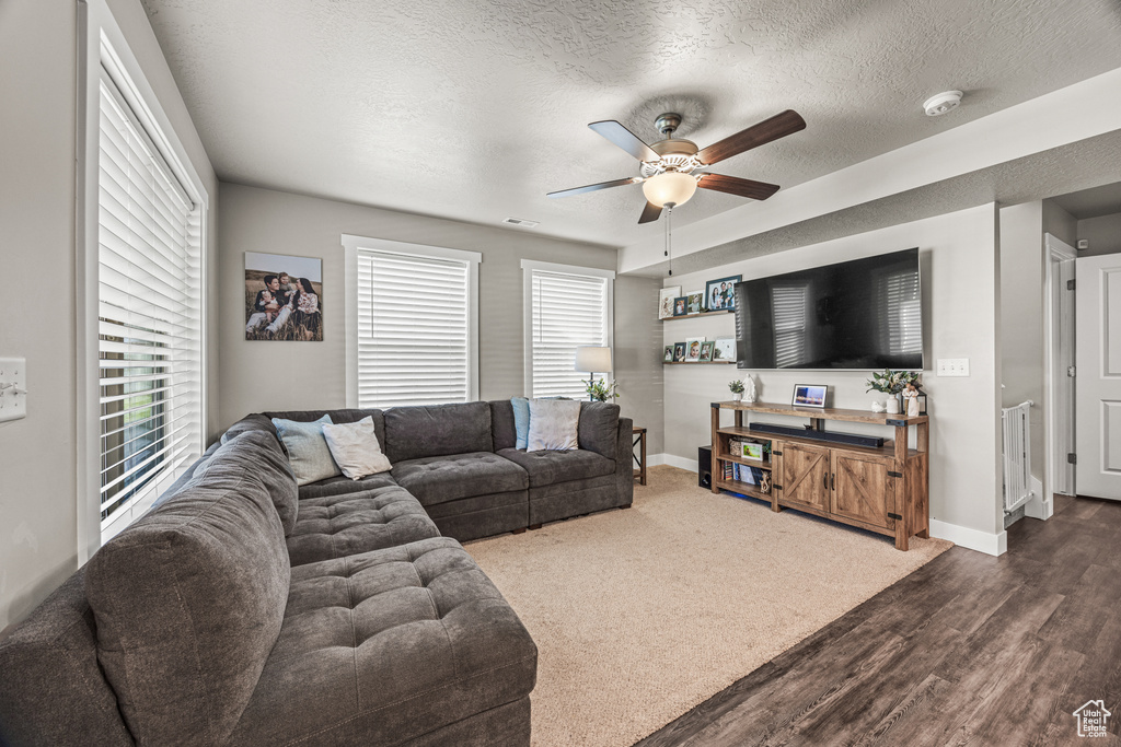 Living room with a textured ceiling, dark carpet, and ceiling fan