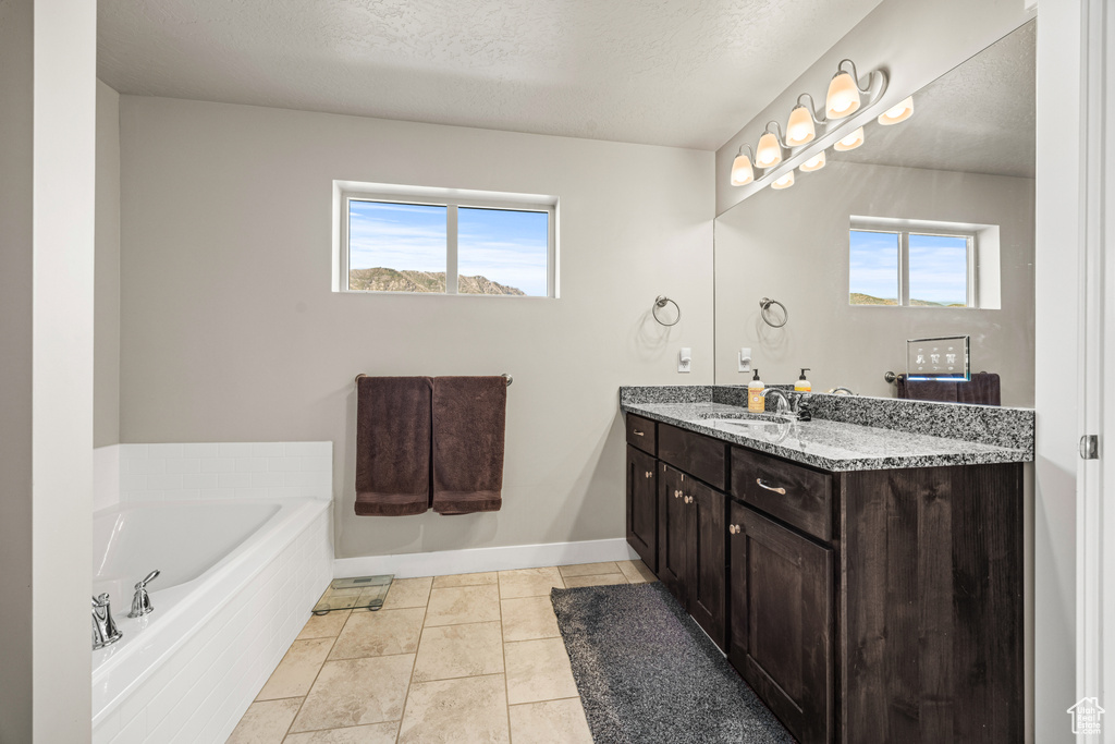 Bathroom featuring a textured ceiling, plenty of natural light, tiled tub, and vanity