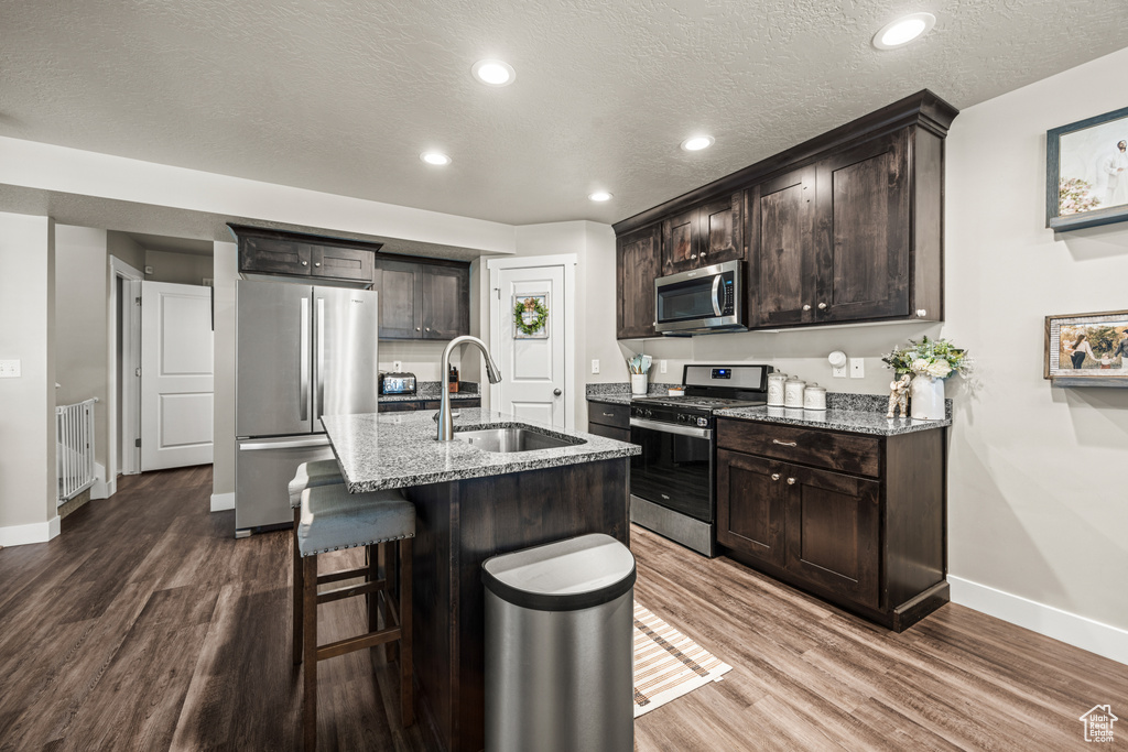 Kitchen featuring appliances with stainless steel finishes, hardwood / wood-style flooring, light stone countertops, and dark brown cabinetry