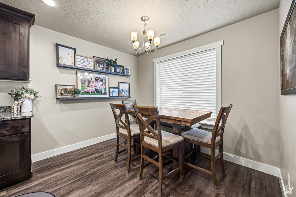 Dining room with dark wood-type flooring, a textured ceiling, and a notable chandelier