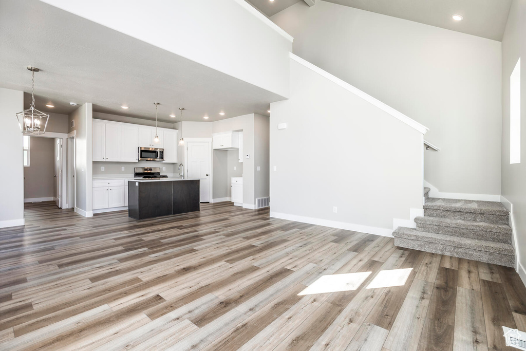 Unfurnished living room featuring light hardwood / wood-style flooring, an inviting chandelier, and a high ceiling