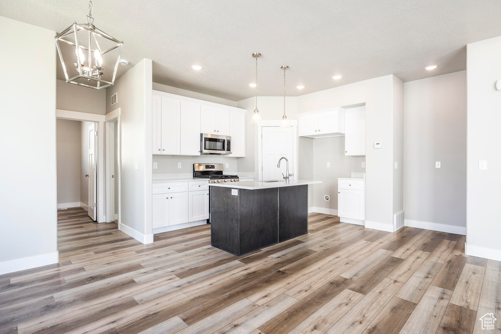 Kitchen featuring white cabinets, hanging light fixtures, light wood-type flooring, stainless steel appliances, and a center island with sink