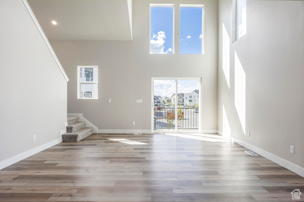 Unfurnished living room with a towering ceiling, plenty of natural light, and light hardwood / wood-style floors