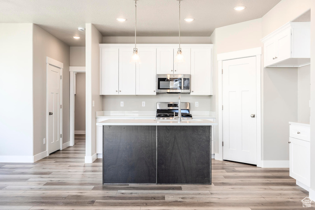 Kitchen with decorative light fixtures, a center island with sink, appliances with stainless steel finishes, light hardwood / wood-style floors, and white cabinets