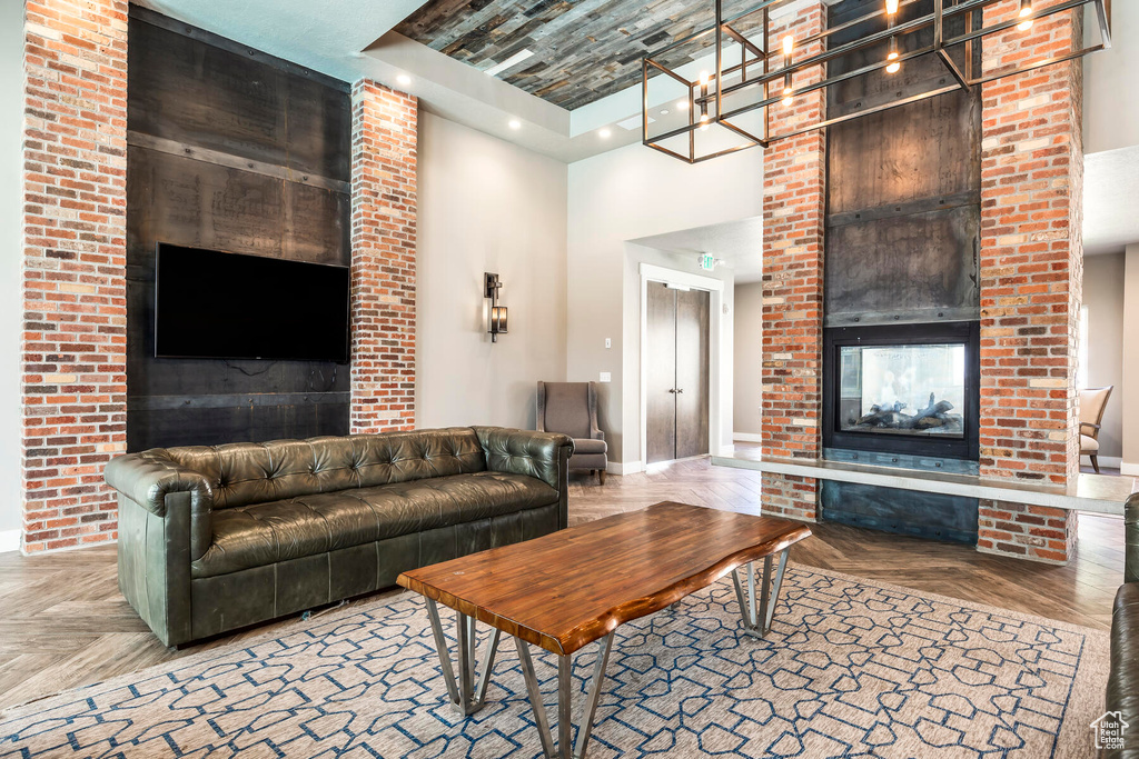 Living room featuring parquet floors, brick wall, a fireplace, a tray ceiling, and a high ceiling