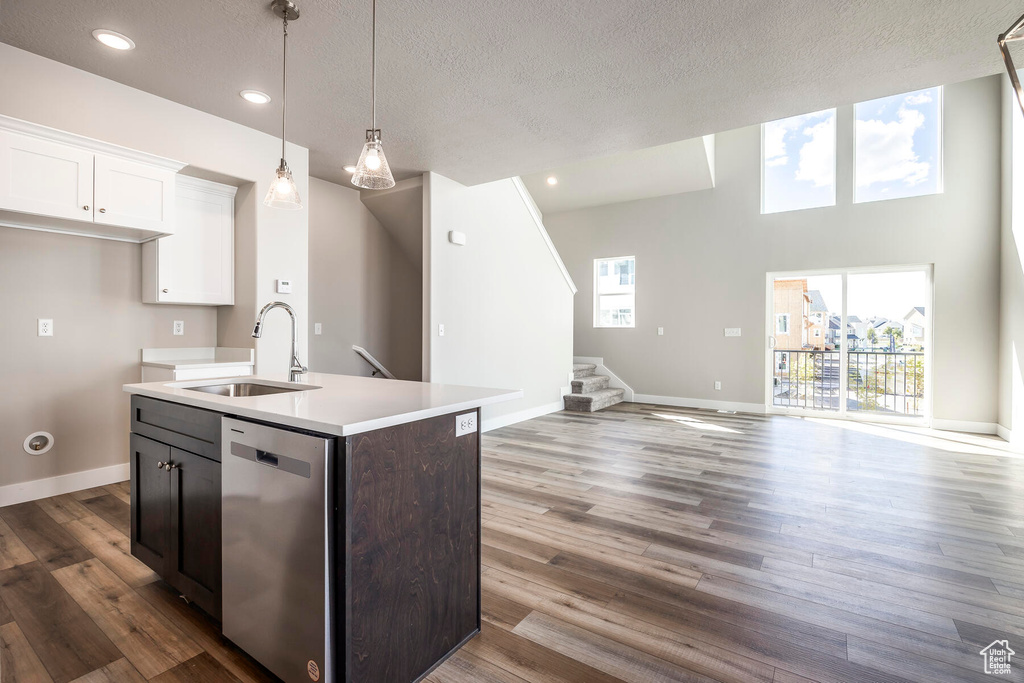 Kitchen featuring a textured ceiling, an island with sink, stainless steel dishwasher, sink, and hardwood / wood-style flooring