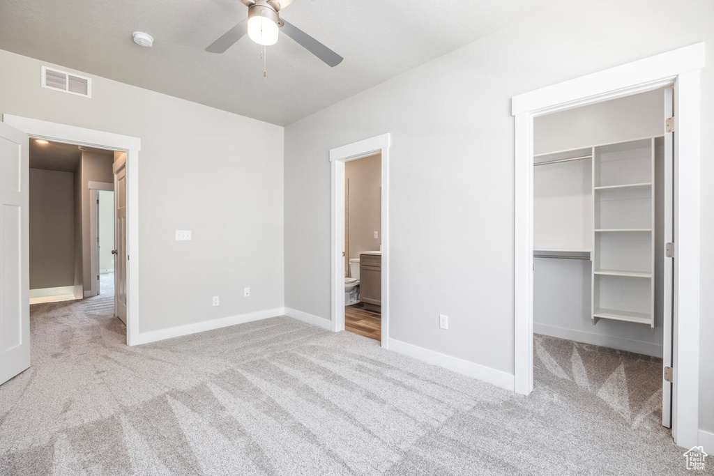 Unfurnished bedroom featuring light carpet, connected bathroom, ceiling fan, a closet, and a walk in closet