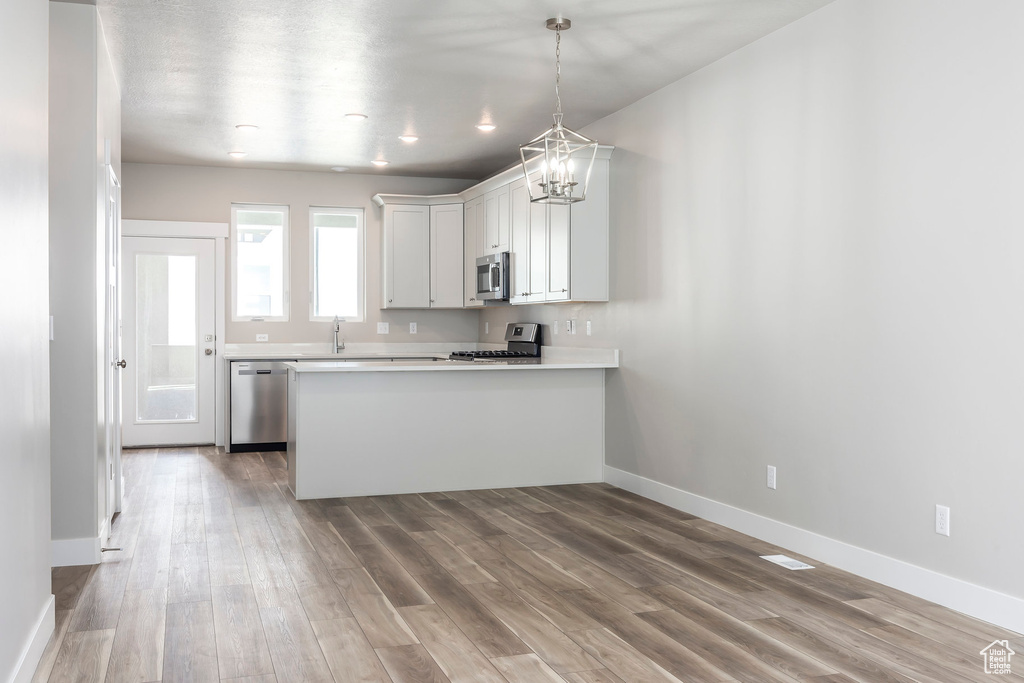 Kitchen with light hardwood / wood-style flooring, kitchen peninsula, appliances with stainless steel finishes, and white cabinets