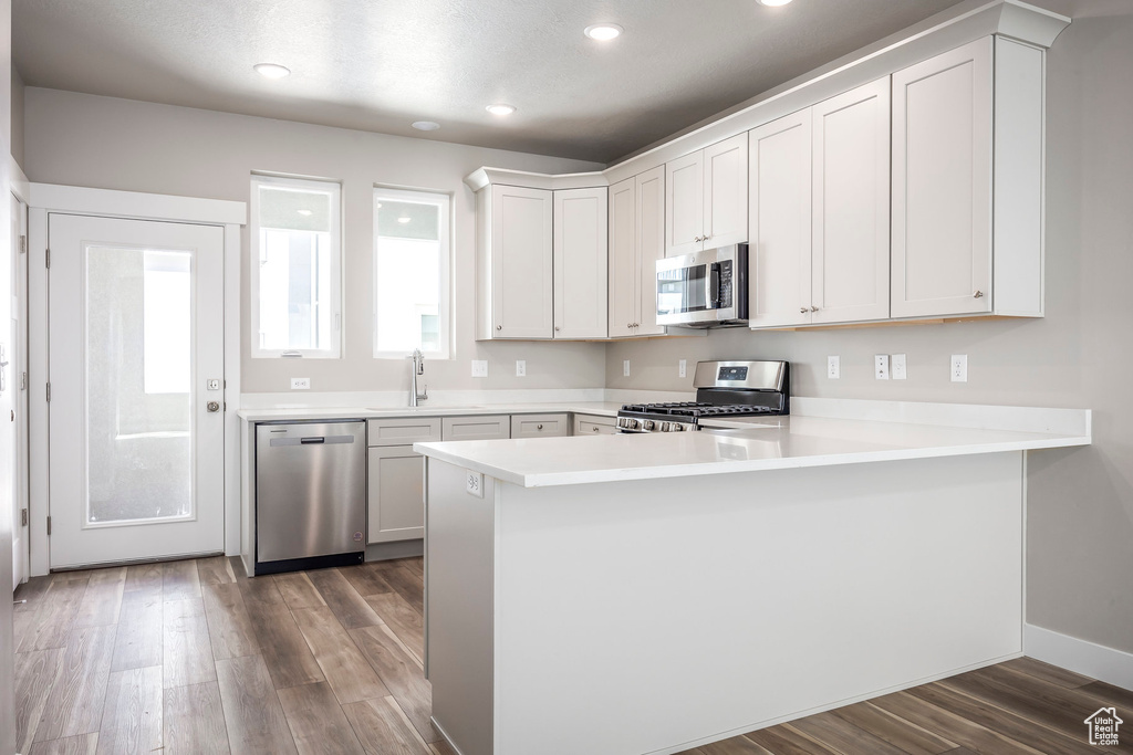 Kitchen featuring appliances with stainless steel finishes, kitchen peninsula, white cabinets, and dark hardwood / wood-style floors