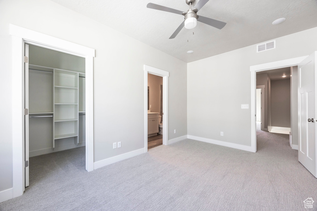 Unfurnished bedroom featuring light carpet, ensuite bath, ceiling fan, and a closet