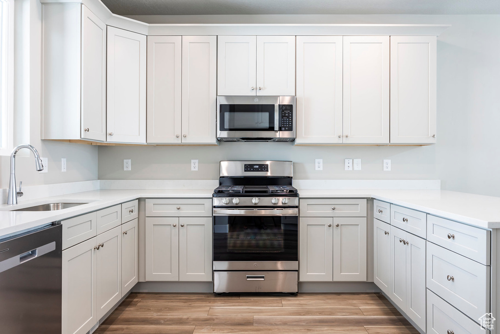 Kitchen featuring light wood-type flooring, appliances with stainless steel finishes, white cabinetry, and sink