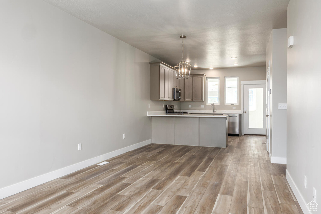 Kitchen with hardwood / wood-style floors, stainless steel appliances, kitchen peninsula, an inviting chandelier, and gray cabinetry