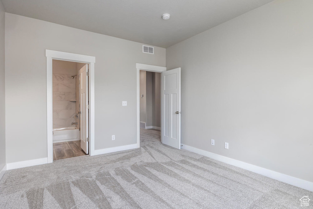 Unfurnished bedroom featuring light colored carpet and connected bathroom