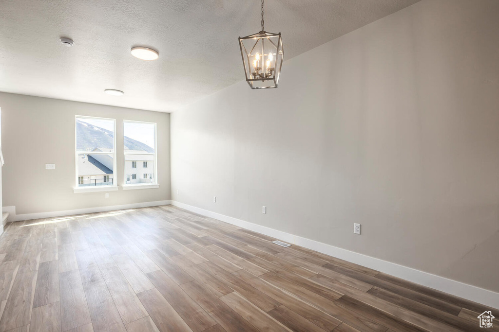 Spare room with wood-type flooring, an inviting chandelier, and a textured ceiling