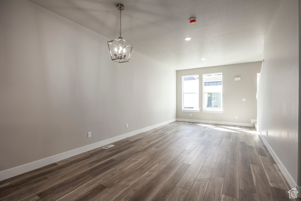 Empty room with dark hardwood / wood-style floors and a chandelier