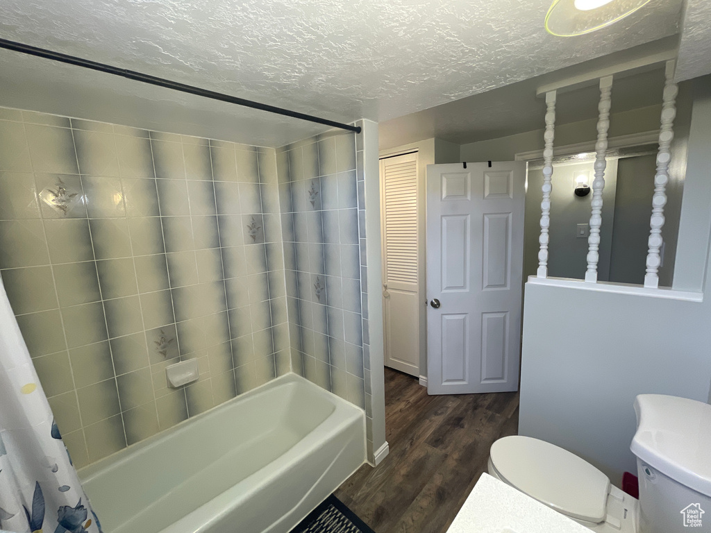 Bathroom featuring a textured ceiling, toilet, shower / tub combo with curtain, and hardwood / wood-style flooring