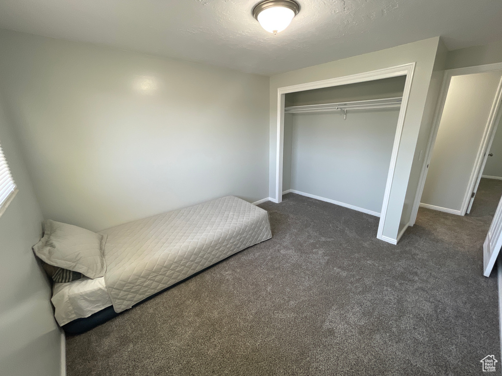 Unfurnished bedroom with a textured ceiling, dark carpet, and a closet