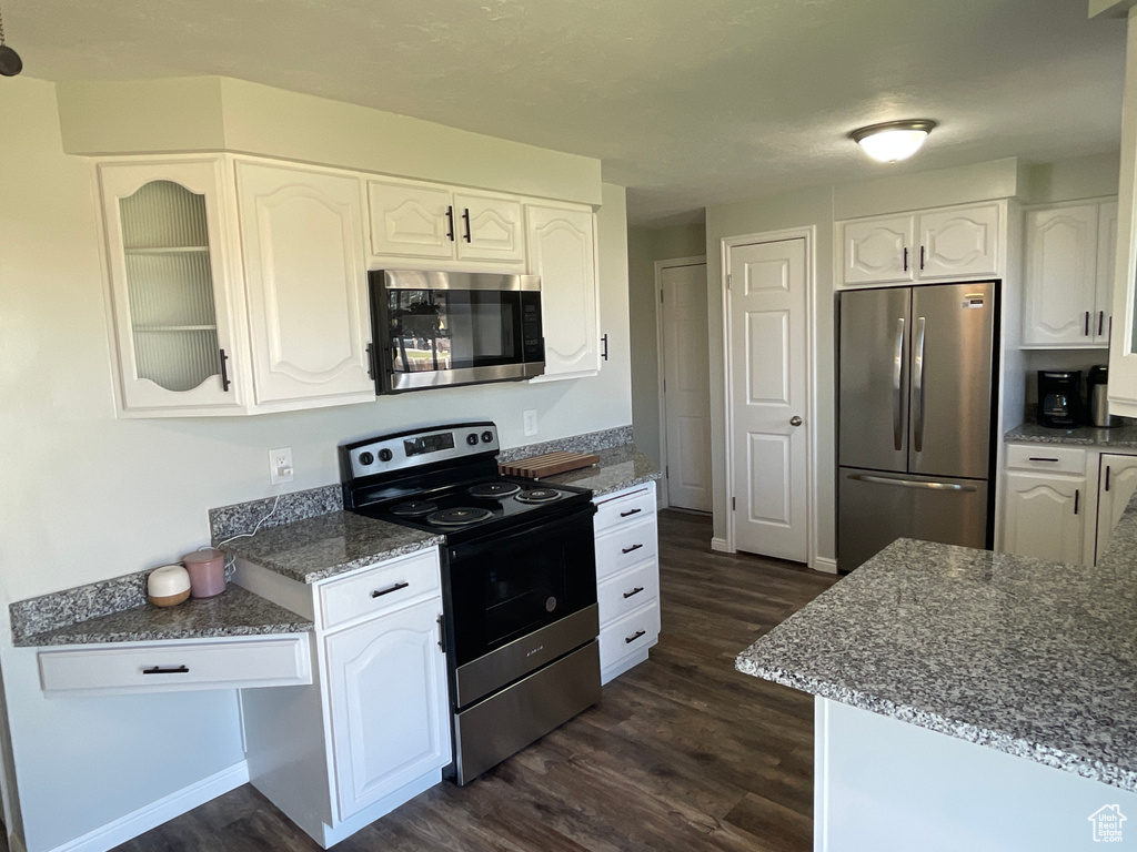 Kitchen featuring dark wood-type flooring, stainless steel appliances, dark stone counters, and white cabinetry