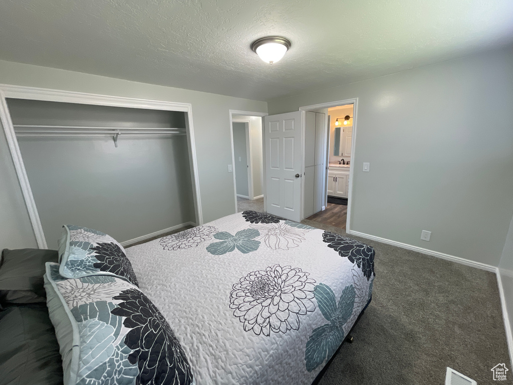 Bedroom featuring a textured ceiling, dark carpet, connected bathroom, and a closet