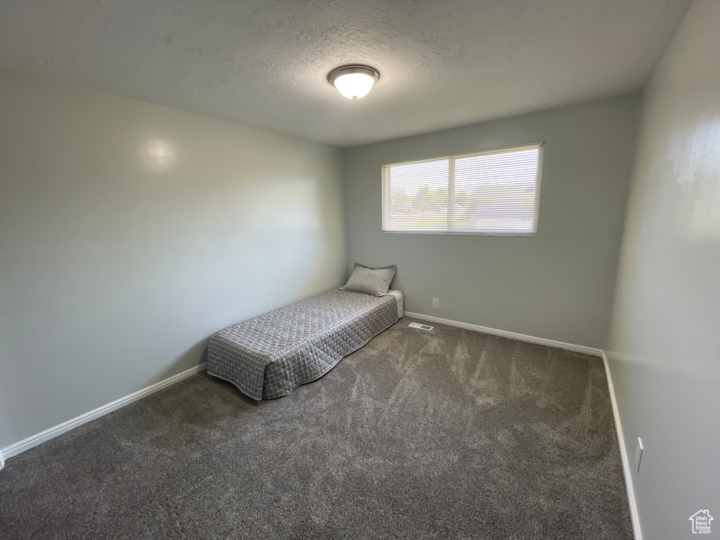 Unfurnished bedroom featuring a textured ceiling and dark colored carpet