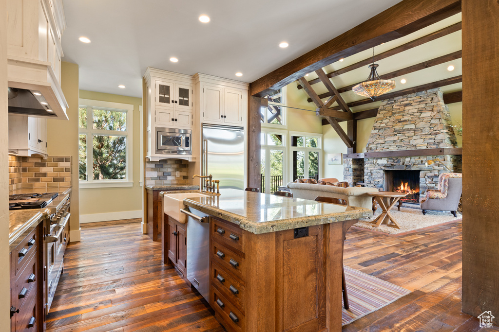 Kitchen featuring built in appliances, dark hardwood / wood-style flooring, a fireplace, backsplash, and beam ceiling