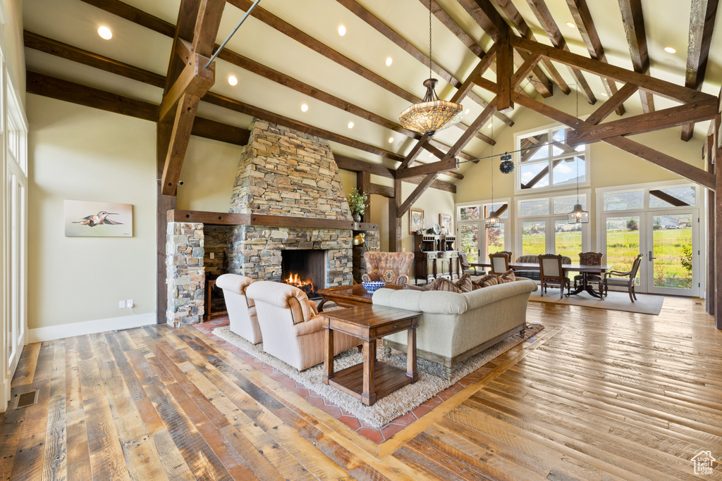 Living room with a fireplace, beamed ceiling, wood-type flooring, and high vaulted ceiling