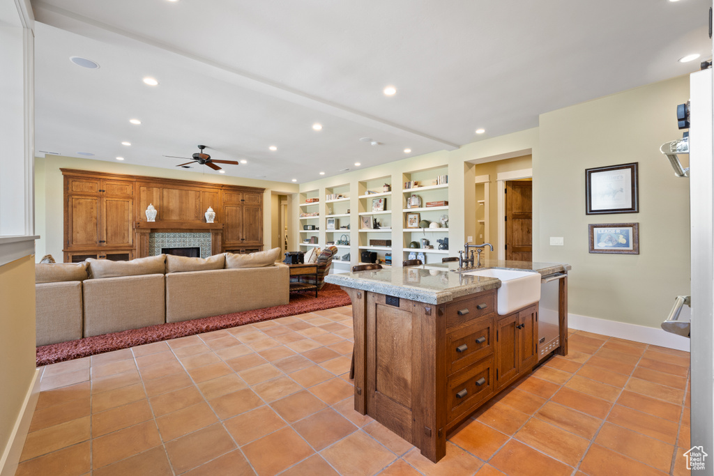 Kitchen with light tile patterned floors, a tiled fireplace, dishwasher, ceiling fan, and a kitchen island with sink