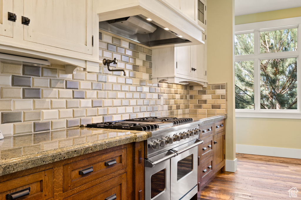 Kitchen featuring range with two ovens, light stone counters, decorative backsplash, dark wood-type flooring, and custom range hood