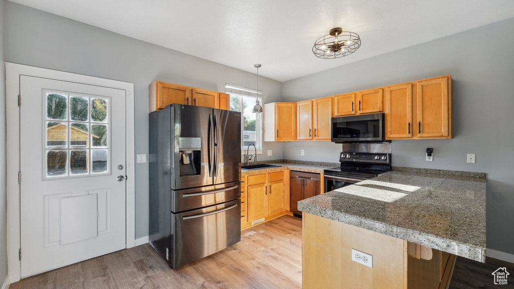 Kitchen featuring light wood-type flooring, appliances with stainless steel finishes, hanging light fixtures, and sink