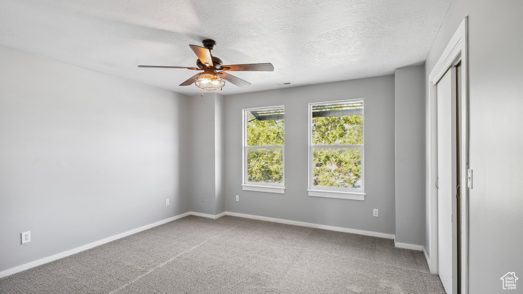 Empty room with a textured ceiling, light colored carpet, and ceiling fan