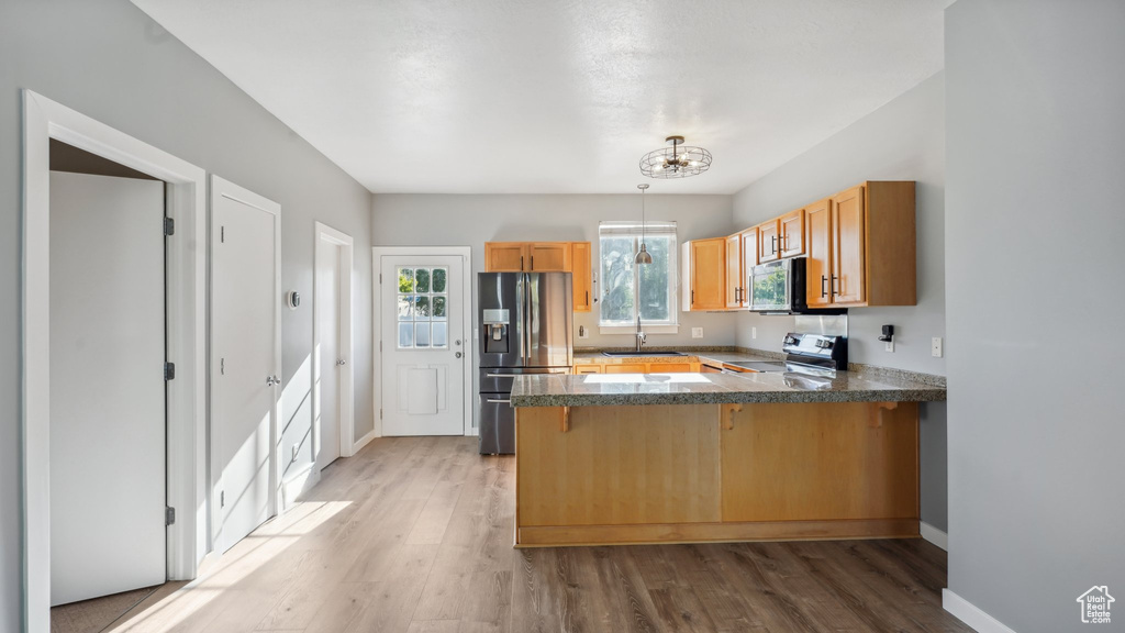 Kitchen with a kitchen breakfast bar, decorative light fixtures, hardwood / wood-style floors, appliances with stainless steel finishes, and kitchen peninsula