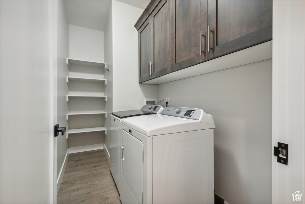 Laundry room with light wood-type flooring, cabinets, and washing machine and clothes dryer