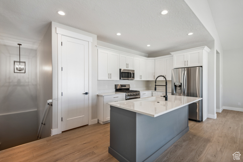 Kitchen featuring an island with sink, stainless steel appliances, white cabinets, and light hardwood / wood-style floors