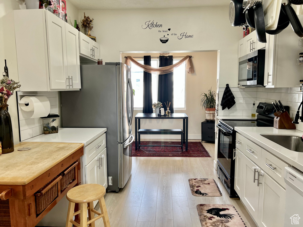 Kitchen with tasteful backsplash, white cabinets, a sink, light countertops, and stainless steel appliances