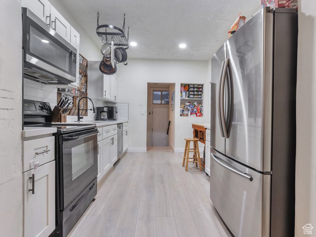 Kitchen featuring a textured ceiling, backsplash, appliances with stainless steel finishes, light wood-type flooring, and white cabinets